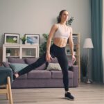 Close-up eines verstellbaren Hometrainer-Fußes mit Fitness-Tracker am Handgelenk im Hintergrund.